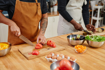 Close up of unrecognizable people cutting vegetables while cooking dinner at home, copy space