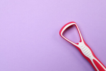 Red tongue cleaner on violet background, top view. Space for text