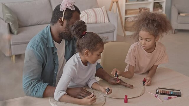 Medium slowmo shot of two funny little African-American girls painting their fathers nails having fun together at home
