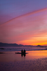 Naklejka na ściany i meble Silhouette shot of a sweet couple enjoying a sunset on the shore in South Korea