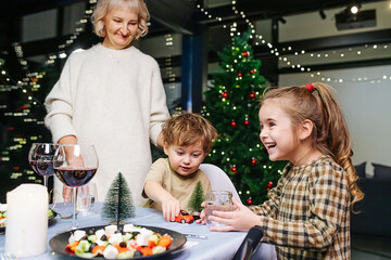 Children sitting at the corner of christams dining table, grandma watching them