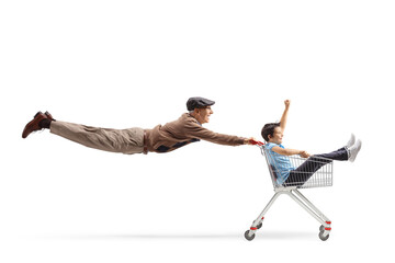 Full length shot of an elderly man flying and pushing a shopping cart with a child inside