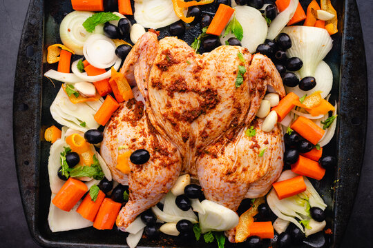 Uncooked Moroccan Spiced Chicken with Roasted Vegetable on a Sheet Pan: Raw spatchcocked chicken with fennel, black olives, carrots, onion, and garlic cloves