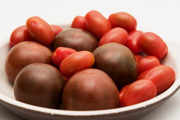 Delicious kumato and cherry tomatoes piled on a clay plate over white background.