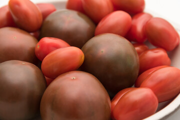 Delicious kumato and cherry tomatoes piled on a clay plate over white background.