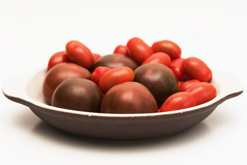 Delicious kumato and cherry tomatoes piled on a clay plate over white background.