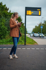 Woman with smartphone is waiting for bus at bus stop.