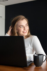 Young woman is smiling and chatting online on a laptop at home or in the office. Concept of studying or working from home online. Resting during work.