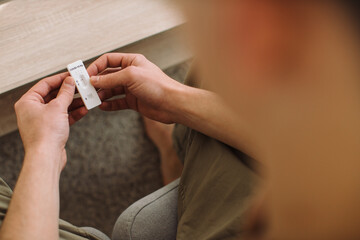 Young man checks for covid-19 test while sitting on sofa at home.