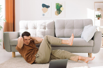 Fototapeta premium Man doing exercise while watching tutorial on laptop at home