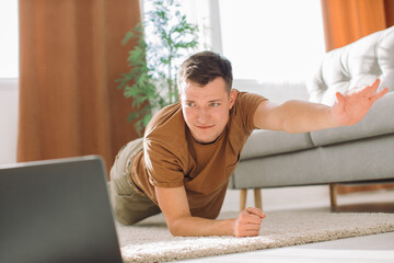 Man doing exercise while watching tutorial on laptop at home