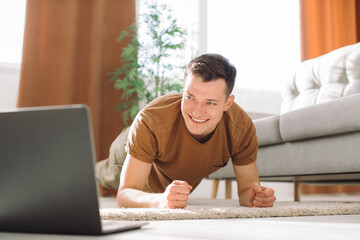Man doing exercise while watching tutorial on laptop at home