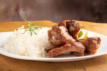 Fried pork ribs, rice and condiments on a white plate arranged on light rustic wood, selective focus.