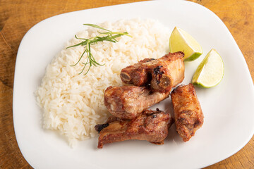 Fried pork ribs, rice and condiments on a white plate arranged on light rustic wood, selective focus.