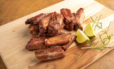 Fried pork ribs with lemon and spices on wood laid out on light rustic wood, selective focus.