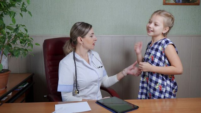 A woman, a pediatrician, examines a girl patient. She makes an analysis of the girl's health and speaks to her affably.