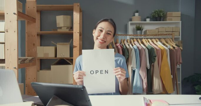 Cheerful attractive young Asian lady with casual smile show open sign in shop reopen from coronavirus pandemic at her cloth shop. Reopening a Business After COVID-19, Excited small business owner.