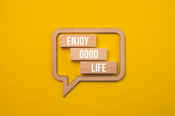 Wooden blocks with the words ENJOY GOOD LIFE in speech bubble. Text sign showing Enjoy Good Life on a beautiful yellow background. Close up. Copy space.