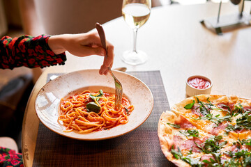 Woman eats Italian pasta with tomato, meat. Close-up spaghetti Bolognese wind it around a fork with a spoon. Parmesan cheese