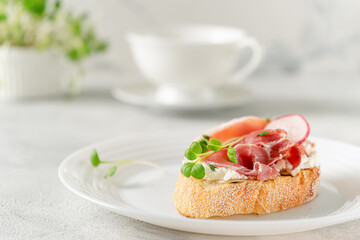 Mediterranean appetizer. Open sandwich with prosciutto or jamon on white plate. Copy space