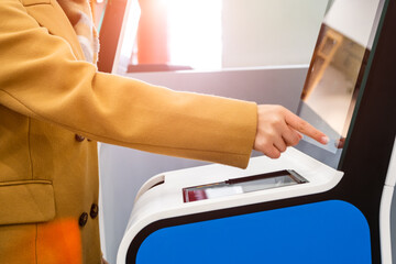 Woman passenger uses self service kiosk with touchscreen to check-in for flight to avoid long queue...