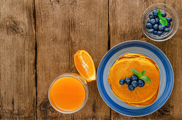 Pumpkin pancakes with blueberries and orange juice on rustic wooden background. Copy space. Overhead