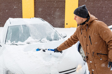A young man cleans snow from his car. Car care in winter