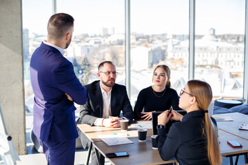 Confident businessman makes a presentation of a new project in the boardroom at a company meeting. Beautiful auditors talk with different partners about the business using a whiteboard and graphs.