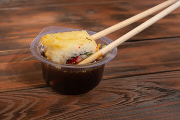 Dipping a delicious roll into a plastic bowl with soy sauce on a wooden table.