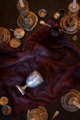 Flat lay view of tipped over silver chalice goblet grail surrounded by vintage candlesticks and miscellaneous vintage metal valuables
