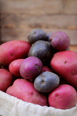 multicolored potatoes in a cloth bag close-up on a wooden background. organic vegetables.