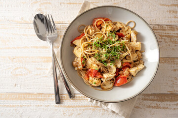 Whole grain spaghetti with tomato, mushroom and chicken strips, garnished with cress, gray plate...