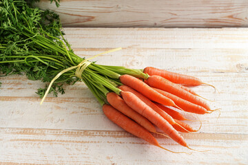 Bunch of organic carrots with green fresh from the market on a light rustic wooden table, copy...