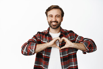 Smiling man showing heart sign, standing in checked shirt over white background