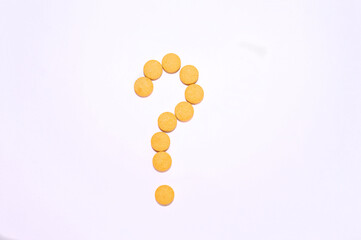 A question mark made of yellow pills. White background. Top view.