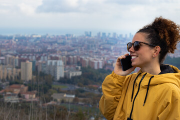 Chica hablando por telefono llamada con chaqueta amarilla con skyline Barcelona de fondo