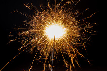 Horizontal dreamy close-up picture of a golden sparkler making many small shiny and hot sparkles on the black background