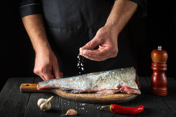 The chef prepares fresh fish sprinkling salt. Preparing to cook fish food. Working environment in the restaurant kitchen