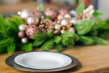 Empty plates on wooden table close-up. Decorated Christmas tree in kitchen. Table setting on New...