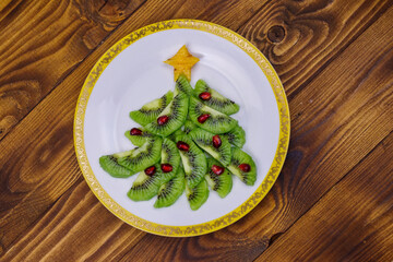 Christmas tree made of kiwi slices and pomegranate on wooden table. Top view. Creative idea for Christmas and New Year festive desserts. Funny food idea for kids