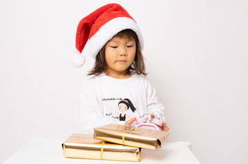 Little asian girl in santa hat sitting with gift boxes isolated over white background.