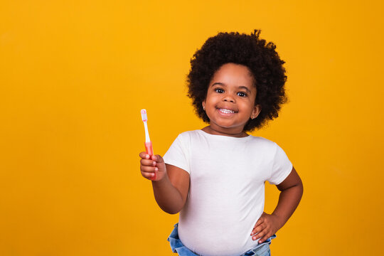 A little cute african american girl brushing her teeth, isolated over yellow background. Healthy teeth concept.