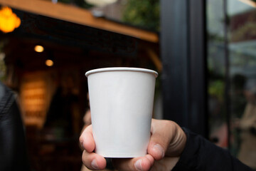 a man holding his hand a white plastic cup. He shows the cup with no brand in his hand. Background is flur.