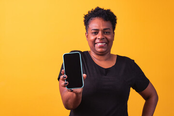 Closeup of smiling afro woman holding smartphone with black blank screen in hand in yellow...