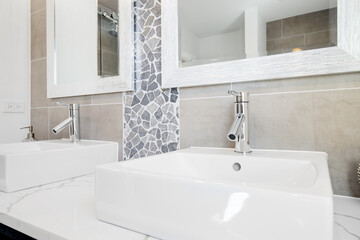 A fancy vessel sink with chrome hardware. A rock and marble back splash cover the wall with a framed mirror also hanging.