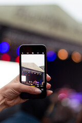 A girl recording a video in the concert area. She wants to create a memory. Music festival area is very colorful. 