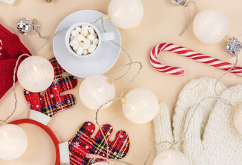 Cup of coffee, gift box and knitted sweater, led lights on beige background. Hygge style, winter concept. Cozy home desk. New year and Christmas celebration mockup. Christmas still life