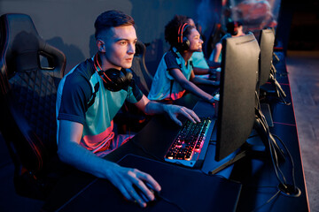Modern cybersport team players sitting in front of computers challenging difficult video game in competition event at internet cafe