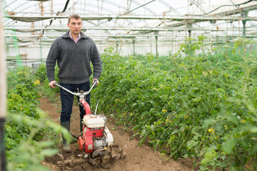 Gardener using motorized cultivator in greenhouse. High quality photo