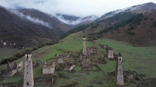 Flying over ancient tower complex Egikal towards cloudy Caucasus mountains. Republic of Ingushetia, Russia